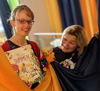zwei Frauen halten Tuecher vor sich und ein Buch