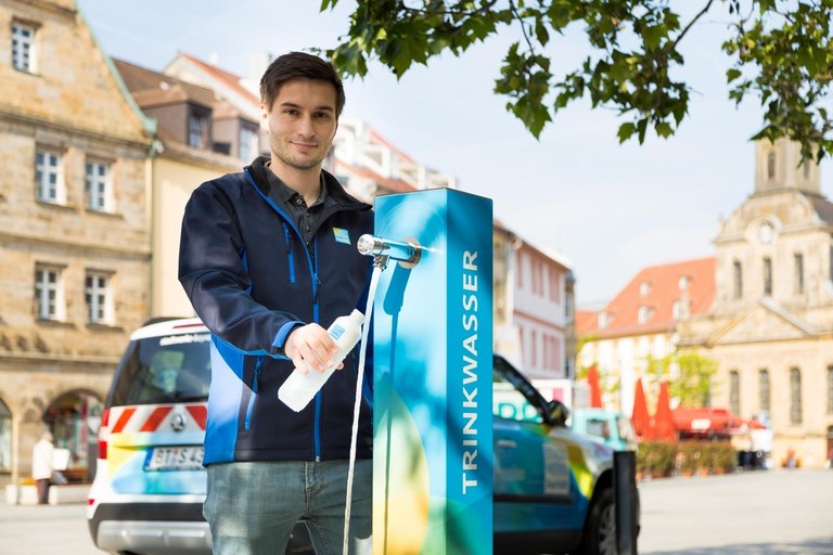 Mitarbeiter der Stadtwerke fuellt Flasche mit Wasser an der Trinkwassersaeule am Bayreuther Markt