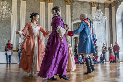 Frauen und Maenner tanzen in historischen Kleidern in einem historischen Raum