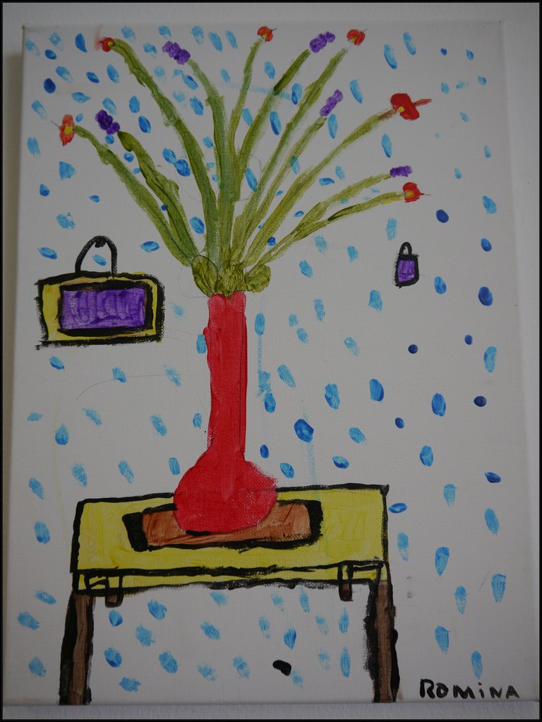 Blumenstrauß in einer roten Vase auf einem Tisch, dahinter ein Bild an der Wand