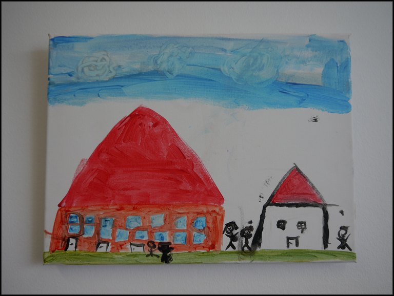 linkes Haus in rot, mit hellblauen Fenstern, rechts ein kleineres Haus in weiß mit rotem Dach, davor mehrere Personen, darueber blauer Himmel
