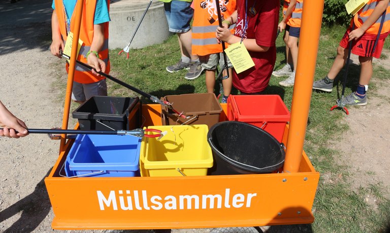 Kinder, die einen Bollwerwagen ziehen und Müll aufsammeln