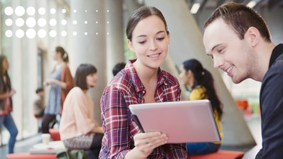 Eine junge Frau und ein junger Mann schauen beide lächelnd auf ein Tablet.