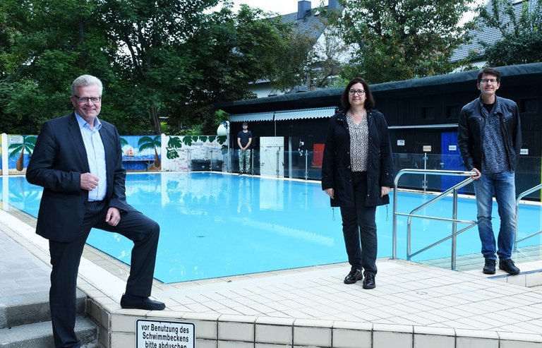 Zwei Maenner und eine Frau stehen vor einem Schwimmbecken  
