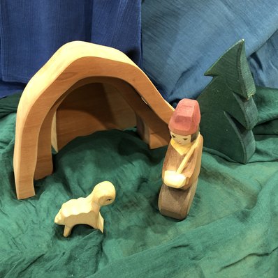 Ein Holzhirte und Holzschaf stehen auf einer grünen Stoffwiese. Im Hintergrund ist ein offener Holzstall.