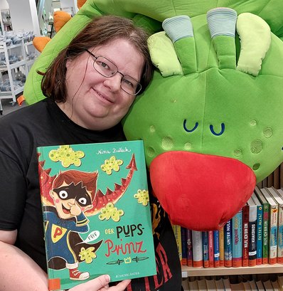 Frau mit einem Buch in der Hand vor einem Plueschdrachen