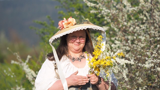 Frau mit Blumenhut und Blumen in der Hand