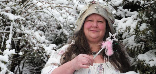 Frau mit Zauberstab in der Hand vor verschneiten Baeumen