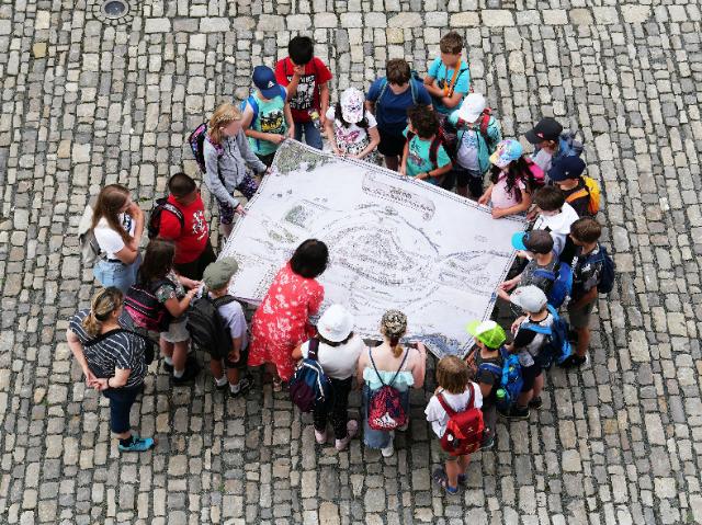 Kinder stehen im Kreis und sehen sich einen Plan an