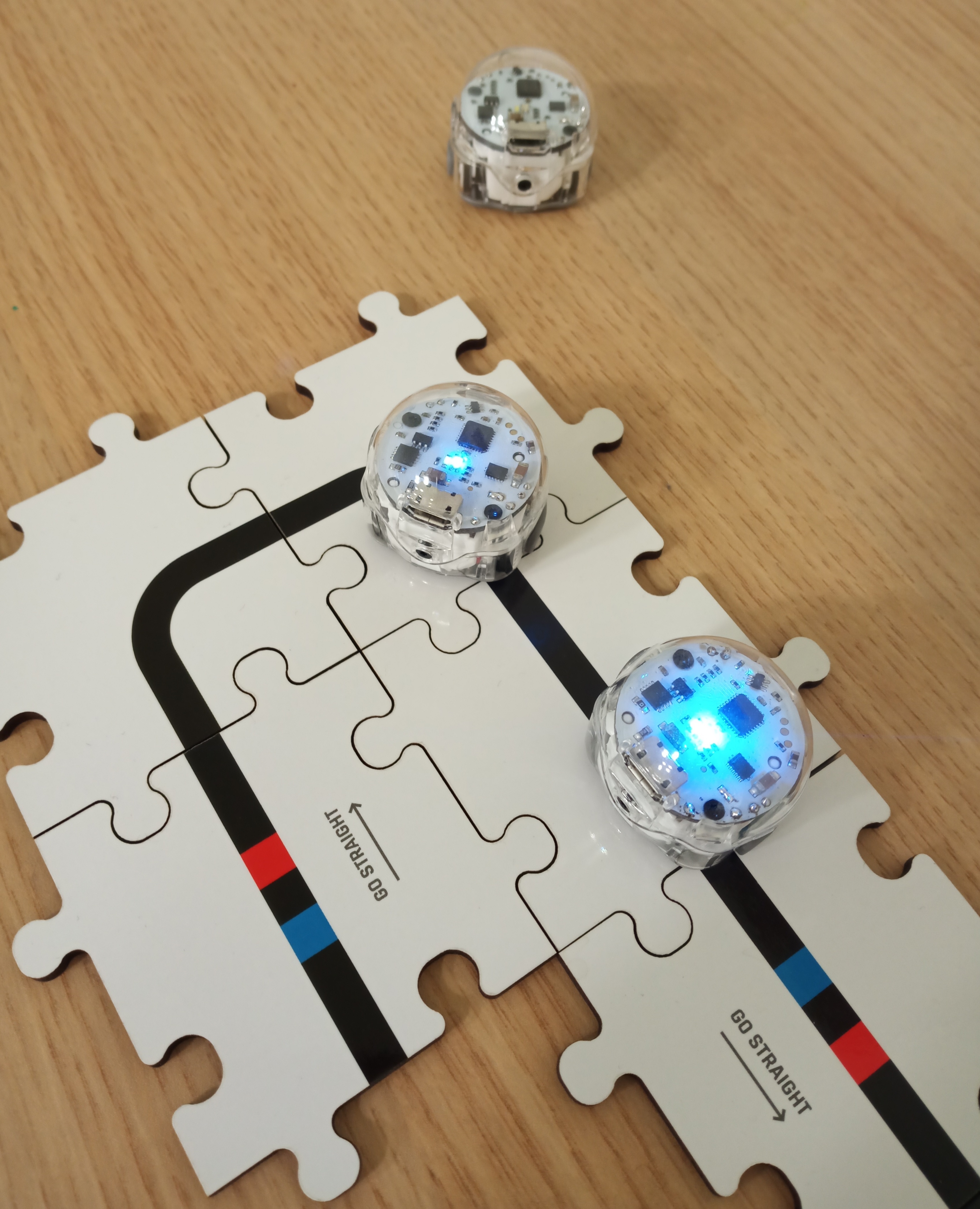 drei kleine Roboter, zwei stehen auf einem Puzzle, der dritte auf einem Tisch