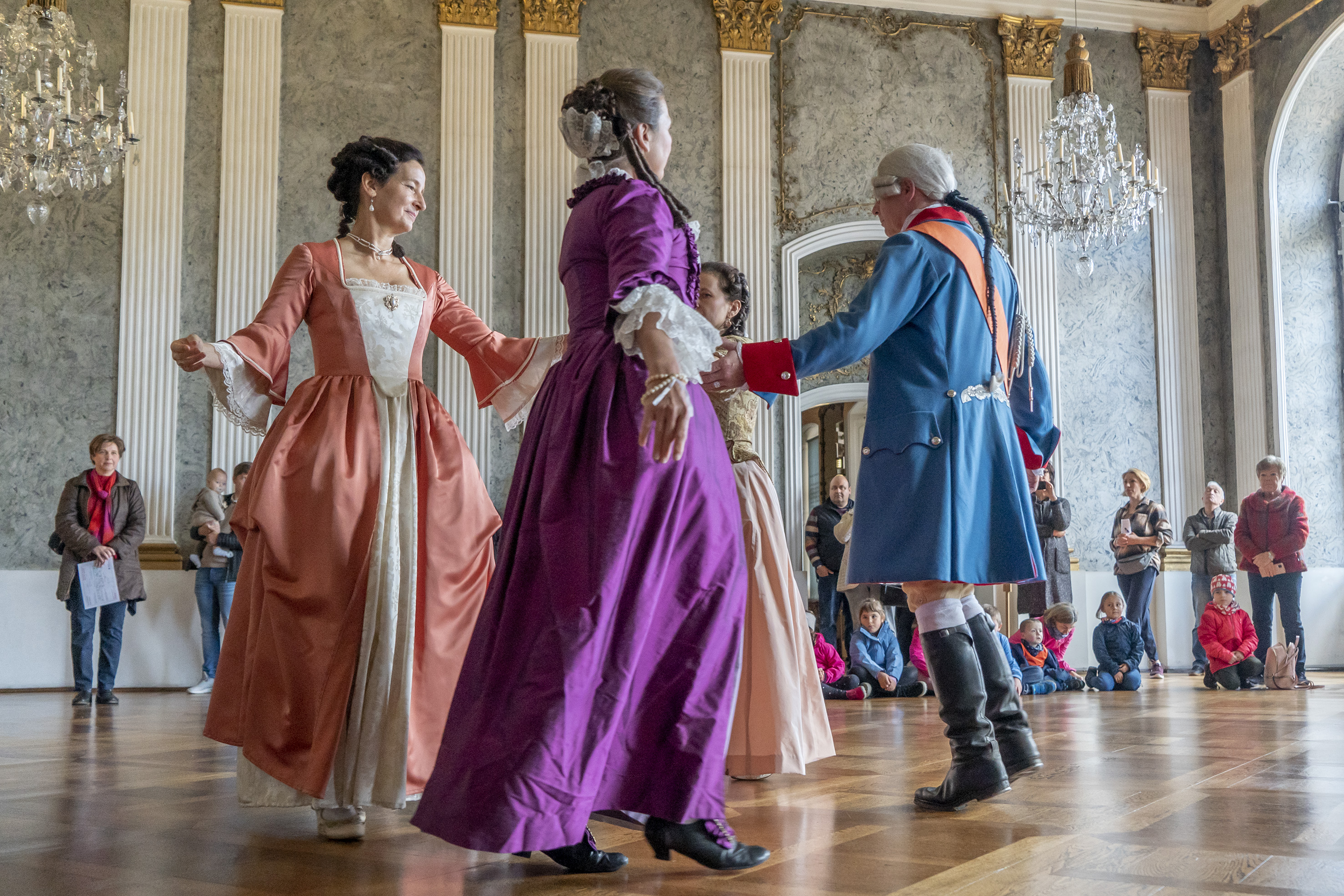 Frauen und Maenner tanzen in historischen Kleidern in einem historischen Raum