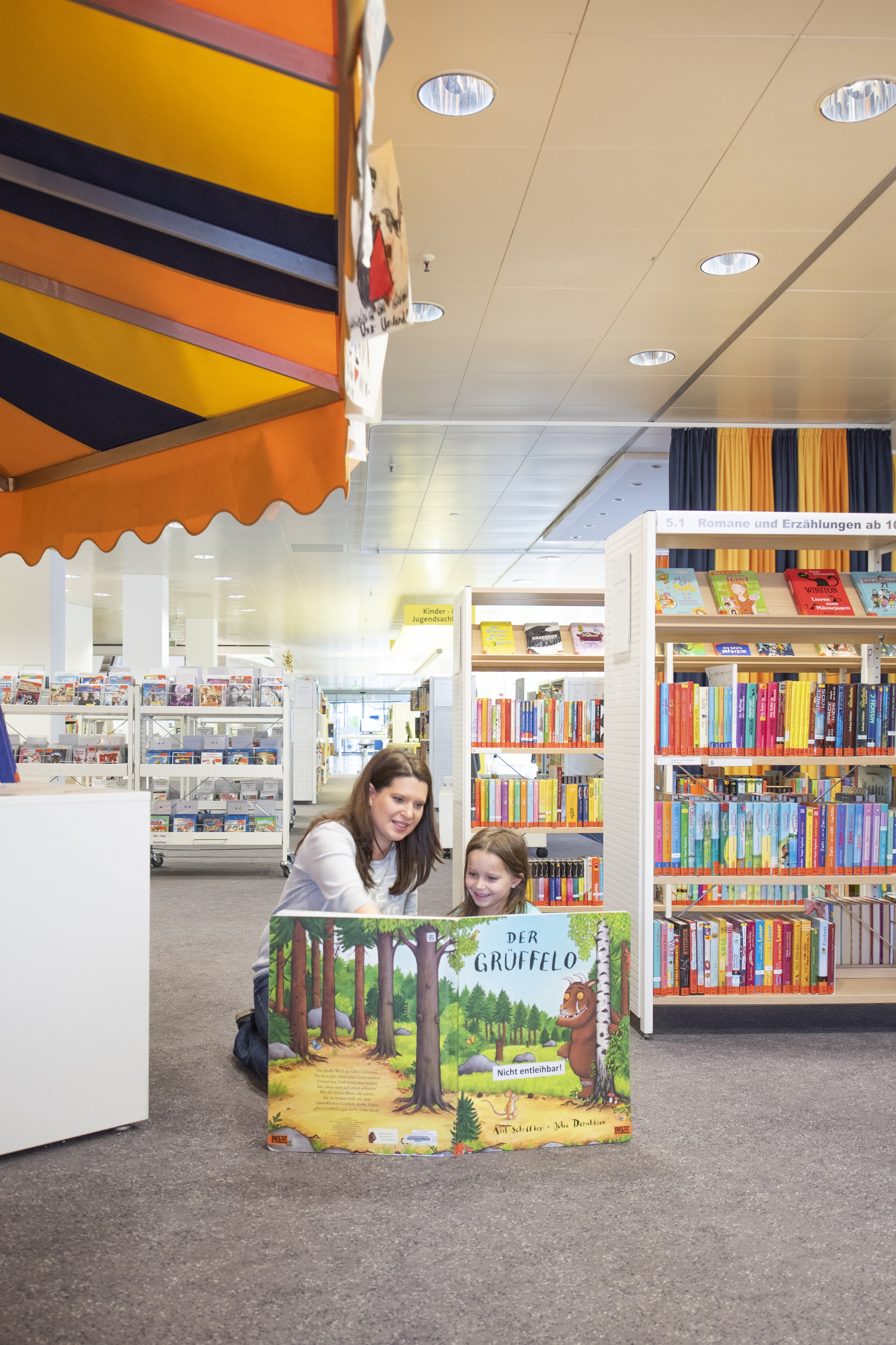 Frau zeigt einem Kind etwas vor einem großen Buch